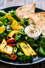 Fresh salad - blue cheese, cherry tomatoes, vegetables and homemade bread on wooden background 