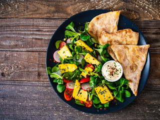 Fresh salad - blue cheese, cherry tomatoes, vegetables and homemade bread on wooden background 