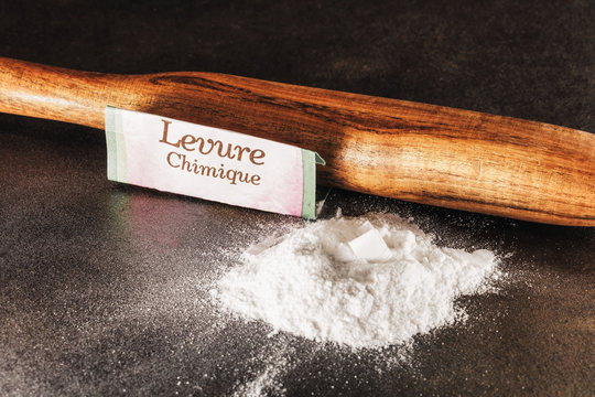 Levure chimique d&eacute;pos&eacute;e en tas sur un plan de travail avec le sachet de levure et le texte "Levure chimique" &eacute;crit en fran&ccedil;ais sur l'emballage et un rouleau &agrave; p&acirc;tisserie en bois  - High key