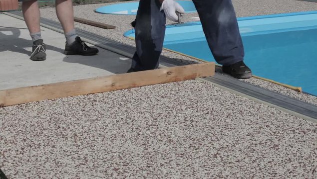 Laying the floor around the outdoor pool. The worker places a stone carpet with resin.
(Shallow DOF).