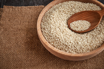 Sesame seeds and a wooden spoon on a dark table. Wooden bowl on canvas . Copy space.