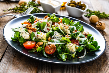 Fresh salad - blue cheese, cherry tomatoes, vegetables and walnuts on wooden background
