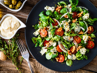 Fresh salad - blue cheese, cherry tomatoes, vegetables and walnuts on wooden background
