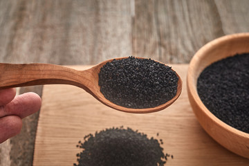 Black cumin seeds and a wooden spoon on a wooden table. Healthy, vegetarian, organic food concept.