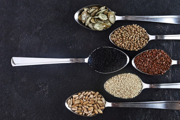 Various Seeds Assortment on dark background. Set of seed: sesame, sunflower, pumpkin, flax, hemp, black cumin in spoons.