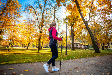 Nordic walking - middle-age woman working out in city park
