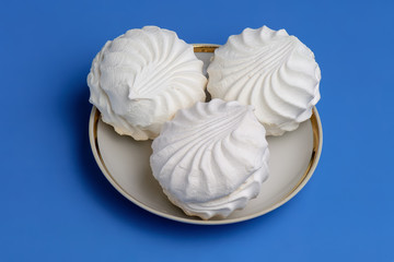 White meringues on plate on blue background. Top view.