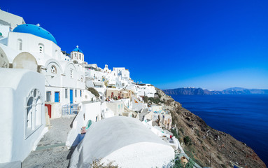 Fototapeta premium Oia typical architecture, Agios Spiridonas and Anastasi Church(blue dome), tower bell in the back, Santorini island, Cyclades, Greece
