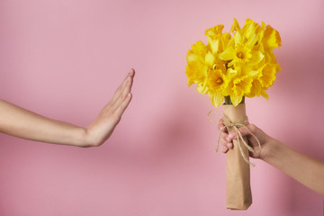 Man's hand gives bouquet of yellow narcissus flowers to girl and receives refusal, woman shows stop sign