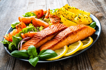 Fried salmon steak with potatoes and vegetables on wooden table
