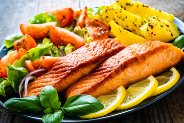 Fried salmon steak with potatoes and vegetables on wooden table
