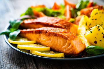 Fried salmon steak with potatoes and vegetables on wooden table
