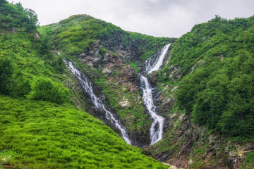 Green mountain range with a waterfall in spring or summer. A mountain range with a waterfall is covered in fog and clouds.
