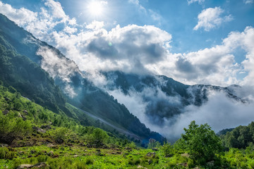 Heavy fog, clouds and bright blue sky with the sun in mountains in the summer or spring. A layer of melting snow in the summer in high mountains.