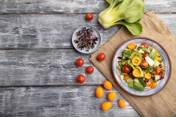 Vegetarian salad of pac choi cabbage, kiwi, tomatoes, kumquat, microgreen sprouts on gray wooden background. Top view, copy space.