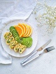 Healthy Breakfast on a round white plate close-up on a light background. Omelet with cheese and herbs, cucumber slices, avocado and orange.