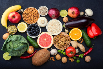 Fruits, vegetables, nuts, mushrooms, chicken and quail eggs and seeds lie on a black concrete table.