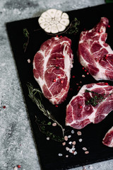 Pork neck on a black board with herbs