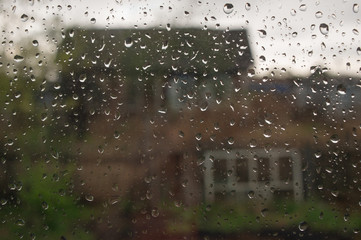 Rainy day in village, summer view from window with raindrops