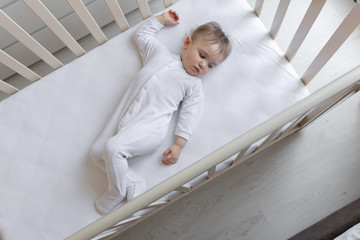 A little girl is smiling as she lies in her children's bed with white sheets. Space for text. On a white background. Copy of the space. Cute little baby lying on the bed, top view.