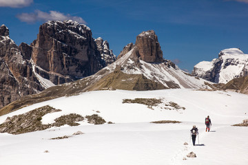Fototapeta na wymiar hikers walking through a snowy landscape and surrounded by large mountains of dolomitic rock in the dolomite alps