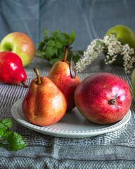 Fruit set on a green tablecloth, apples, pears and mango with sprigs of mint