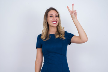 Young caucasian woman standing against gray wall showing and pointing up with fingers number two while smiling confident and happy.