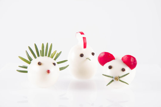 Eggs shaped like animals (with elements made of rosemary, radish, chive) on a white background