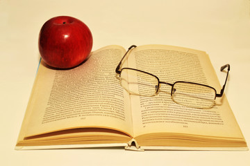 Open book, red apple and reading glasses on book pages