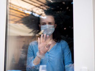 Woman in a medical mask behind a glass window on self-isolation during an epidemic