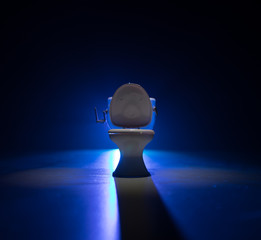 Creative concept. Miniature white toilet bowl on dark foggy background.