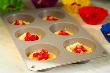 in the process of cooking gluten-free muffins with red currant . raw dough . gray silicone mold for six pieces and small colored bakeware in the background