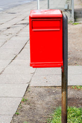 Fototapeta na wymiar a red metal letter box stands on the street during the day in a European country