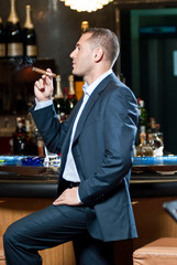 Rich businessman with cigar in lobby bar. Happy man spending free time in restaurant. Luxury concept.