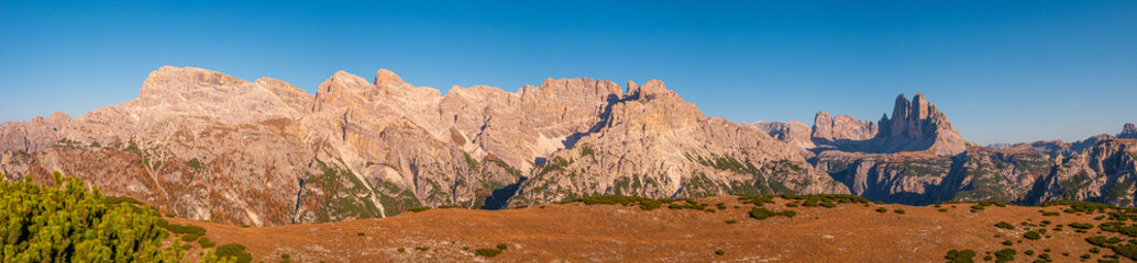 Panoramic view over beautiful sunset in magical Three Dolomite peaks at the national park Three Peaks (Tre Cime, Drei Zinnen) at sunny day and blue sky, South Tyrol, Italy, wide angle