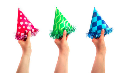 A set of colorful party cap made of paper, hold in a hand, isolated on white background. Pink, green and blue holiday cup, carnival accessory with tinsel.