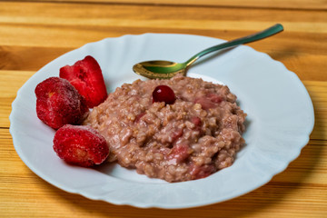 plate with oatmeal with strawberries on a wooden table