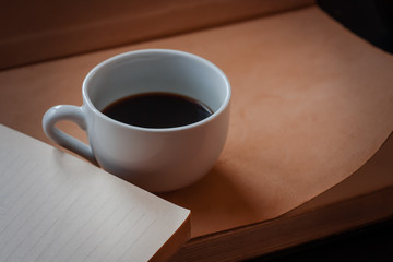 Cup of hot fragrant black morning coffee stands on a open book. Light brown warm colors. Selective focus