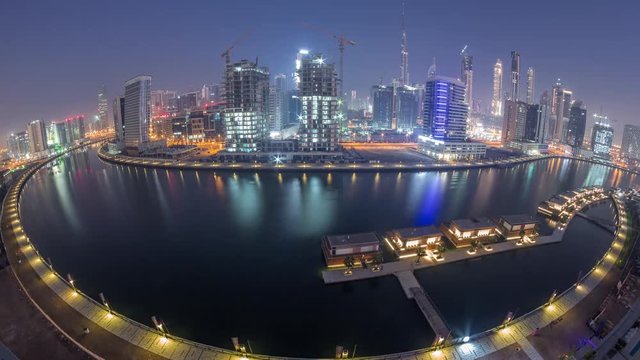 Panorama of the modern city during all night timelapse with lights switching off. Aerial view of graceful canal and luxury skyscrapers in Business Bay, Dubai, United Arab Emirates