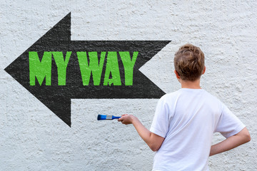 Ein blonder Junge vor einer Wand mit schwarzem Pfeil und dem grünen Text MY WAY