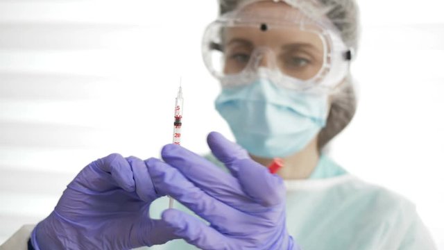 Portrait of a beautiful nurse in a protective suit with a syringe in her hands.