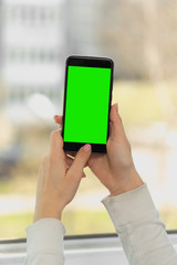 female hand holds a smartphone with a green screen, chromakey. close up on a light background.vertical shot