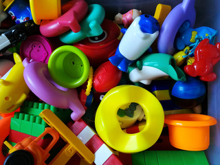 Multi-colored plastic children’s toys piled in a box. Top view. 
Consumer society concept