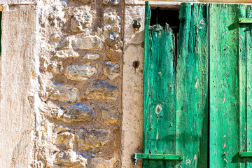 Authentic house with a stone wall, with beautiful old open windows and with green shutters, and with vases on the window.