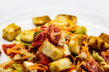 Salad with meat of pig, tomatoes, carrots, cabbage and crackers with bread runner with sauce on the white plate. Healthy and tasty meal for the diet. Delicious breakfast or lunch without GMO