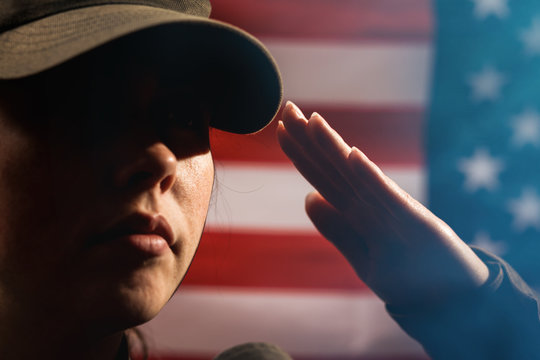 Memorial day. A female soldier in uniform salutes against the background of the American flag. Close-up portrait. Copy space. The concept of the American national holidays and patriotism
