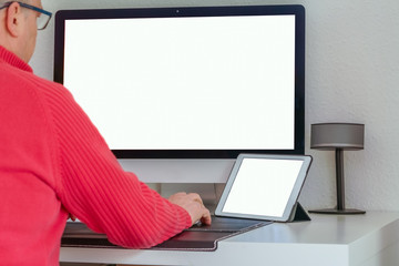 Old man working on tablet and computer at the desk. Tablet and computer screen mockup.