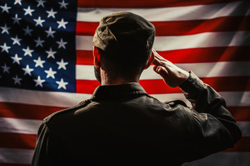 Memorial day. A uniformed soldier salutes against the background of the American flag. Rear view....