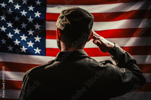 Memorial day. A uniformed soldier salutes against the background of the American flag. Rear view. Dark colors. The concept of the American national holidays and patriotism