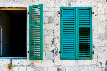 Authentic house with a stone wall, with beautiful old open windows and with green shutters, and with vases on the window.